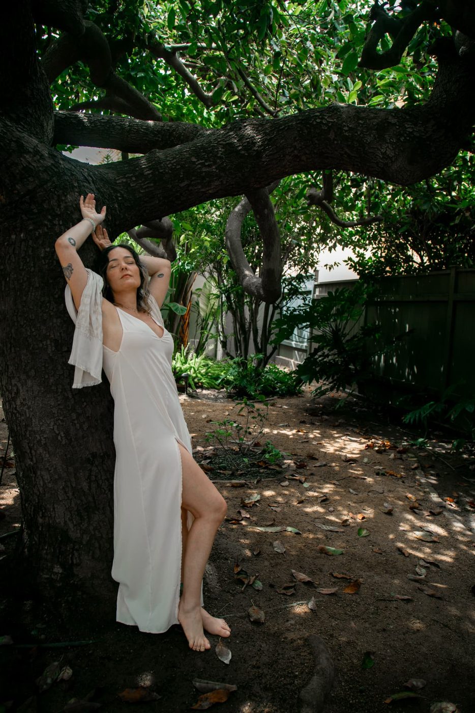 Simone Dib leaning against a tree, eyes closed, arms raised